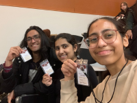 A picture of Batool with her two friend. All three of them in the picture are holding a Ellehacks 'Hacker' card on thier hand, while smiling.